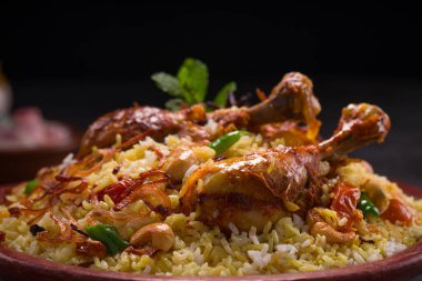 Jeera pilavı ve baharat kullanarak tavuk dhum biryani gri arka planda raitha ve limon turşusu eşliğinde toprak malzemesi..