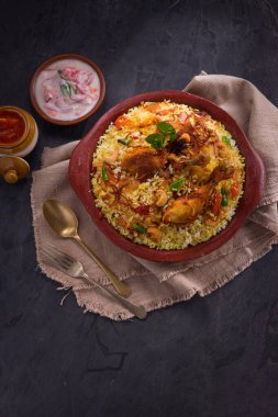 Jeera pilavı ve baharat kullanarak tavuk dhum biryani gri arka planda raitha ve limon turşusu eşliğinde toprak malzemesi..