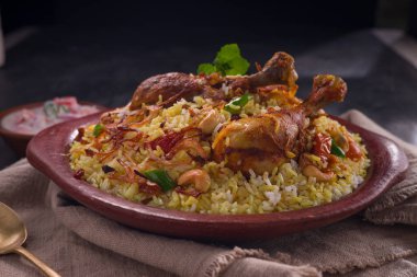 Jeera pilavı ve baharat kullanarak tavuk dhum biryani gri arka planda raitha ve limon turşusu eşliğinde toprak malzemesi..