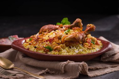 Jeera pilavı ve baharat kullanarak tavuk dhum biryani gri arka planda raitha ve limon turşusu eşliğinde toprak malzemesi..