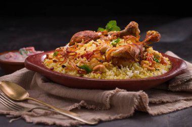 Jeera pilavı ve baharat kullanarak tavuk dhum biryani gri arka planda raitha ve limon turşusu eşliğinde toprak malzemesi..