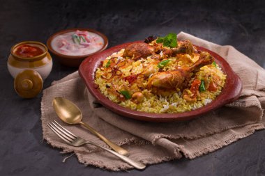 Jeera pilavı ve baharat kullanarak tavuk dhum biryani gri arka planda raitha ve limon turşusu eşliğinde toprak malzemesi..
