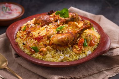 Jeera pilavı ve baharat kullanarak tavuk dhum biryani gri arka planda raitha ve limon turşusu eşliğinde toprak malzemesi..