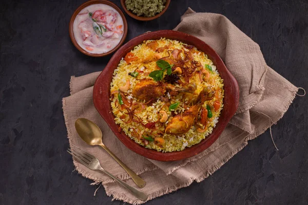 Jeera pilavı ve baharat kullanarak tavuk dhum biryani gri arka planda raitha ve limon turşusu eşliğinde toprak malzemesi..