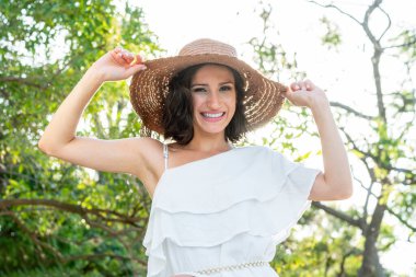 Parkta rahat ve mutlu bir kadın, ışığa karşı büyük bir gülümseme, Whit şapka