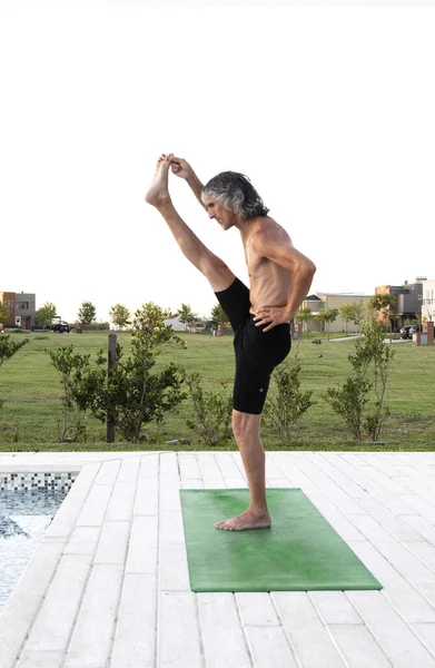 Bir evin bahçesinde yoga egzersizi yapan bir adam.