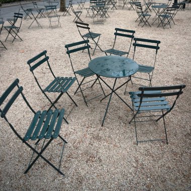 Yağmurdan sonra halka açık bir parkta ıslak bir masanın etrafında yeşil sandalyeler.