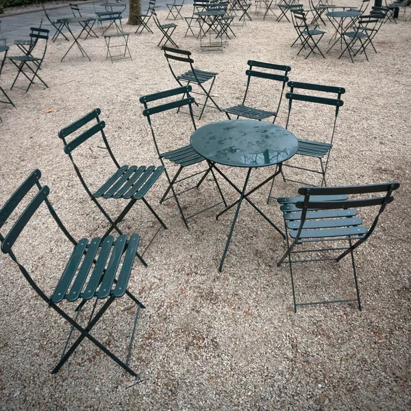 Yağmurdan sonra halka açık bir parkta ıslak bir masanın etrafında yeşil sandalyeler.