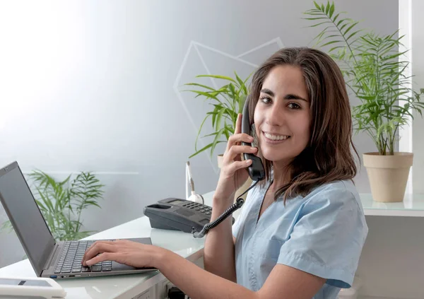 Diş hekimliği resepsiyonunda çalışan genç bir hemşire telefonda konuşuyor ve gülümsüyor.