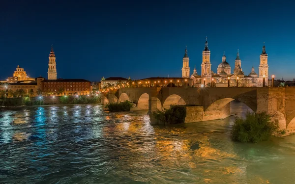 Bazilika Panny Marie pilíř v Zaragoze a most ve Španělsku v noci — Stock fotografie