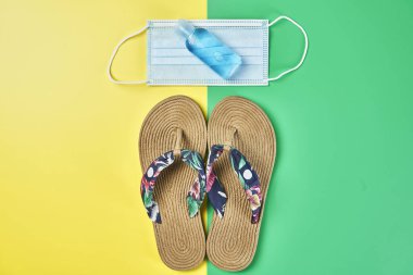 Stüdyo fotoğrafı, tam boy sandaletler iki renk sarı ve yeşil dikey arka plan, antiseptik jel ve yüz maskesi tatil için hazır.