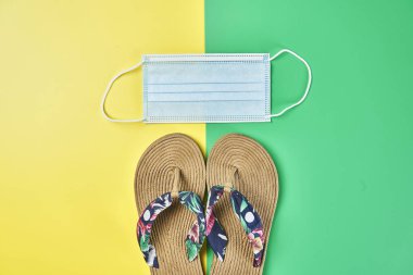 Stüdyo fotoğrafı, iki renkte yaz sandaletleri sarı ve yeşil dikey arka plan ve yüz maskesi tatil için hazır.