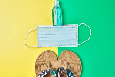 Stüdyo fotoğrafı, iki renk üzerinde yaz sandaletleri sarı ve yeşil dikey arka plan, antiseptik jel ve yüz maskesi tatil için hazır.