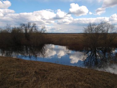 Nehir manzarası üzerinde gökyüzünde beyaz kümülüs bulutları, suyun üzerinde büyük bulut yansıması, manzaralı bahar deniz manzarası.
