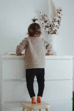 Küçük bir kız çocuğu beyaz tuvaletin yanında dikiliyor.