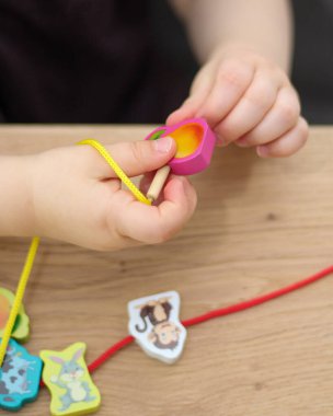 Çocukça ellere yakın durun. Çocuk ipin ucuna boncuk takıyor. Güzel motor beceri geliştirme. Erken eğitim, Montessori Yöntemi, Çocuk Geliştirme.