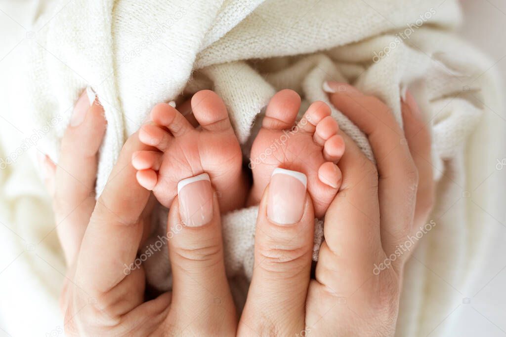Feet of the newborn in the hands of the mother. Mother holds babys feet in her hands. Happy family concept.