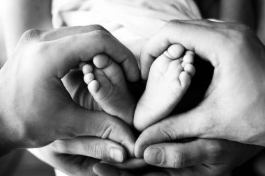 Çocukların ayakları beyazın üzerinde anne ve babanın ellerinde. Anne, baba ve yeni doğan çocuk. Mutlu Aile İnsanları konsepti. Siyah ve beyaz.