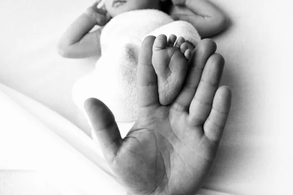 Pieds de bébé dans la main des pères. Le petit pied d'un nouveau-né entre les doigts d'une main de parents. Palme ouverte et petits orteils. Photographie noir et blanc. — Photo