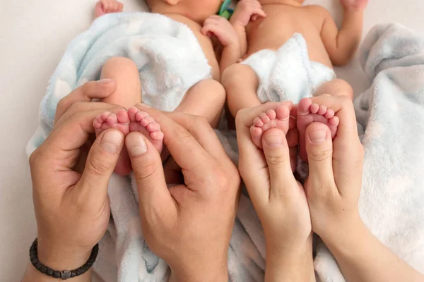 Baba ve anne yeni doğan ikizlerin bacaklarını tutuyor. Ebeveynlerin elleri ve çocuklarının ayakları.. — Stok fotoğraf