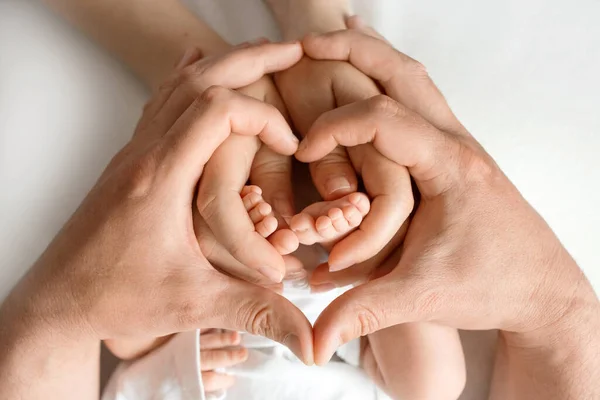 Primer plano. piernas de un bebé recién nacido en manos de mamá y papá. manos adultas sostienen los pies del bebé en la forma de un corazón. Imagen con enfoque selectivo — Foto de Stock