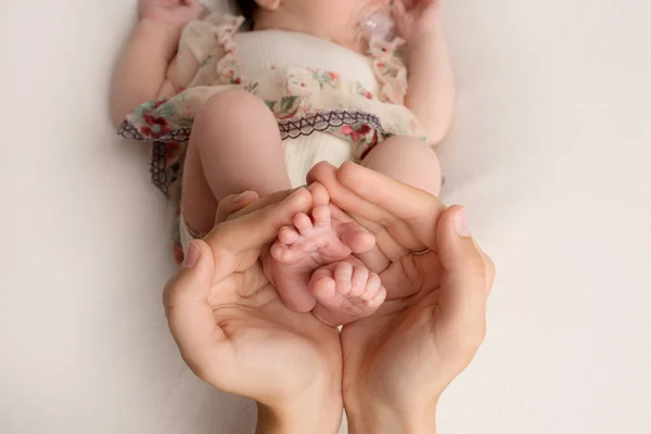 Vrouwelijke handen van jonge moeder houden haar pasgeboren baby voeten, close-up beeld met wazig baby op de achtergrond — Stockfoto