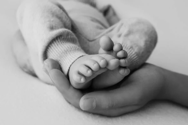 Mani femminili di giovane madre che tiene i piedi del neonato, immagine primo piano con bambino sfocato sullo sfondo — Foto Stock