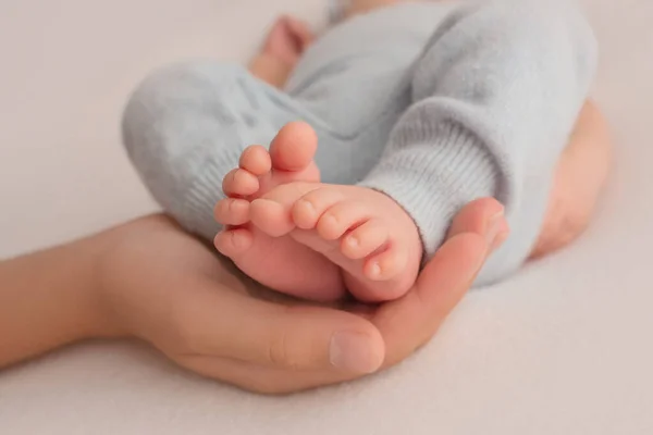 Kvinnliga händer ung mor håller hennes nyfödda barn fötter, närbild bild bild med suddig baby i bakgrunden — Stockfoto
