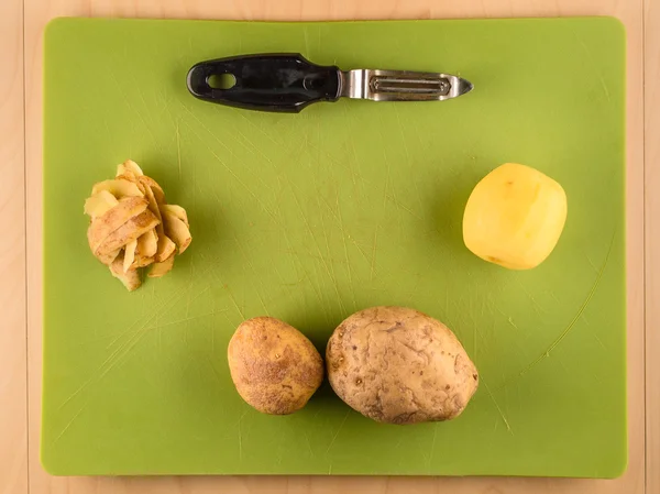 Potatoes and skins on green plastic board — Stock Photo, Image