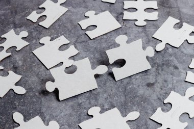 Yakın çekim beyaz testere desenli yapboz parçaları, kayıp parçalarla ilişkilendirilecek. Düz bir zeminde farklı doku ve kağıt aksesuarları ile yerleştirilmiş.