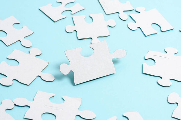 Close-Up White Jigsaw Pattern Puzzle Pieces To Be Connected With Missing Last Piece Positioned On A Flat Lay Background With Different Texture And Paper Supplies Accesories