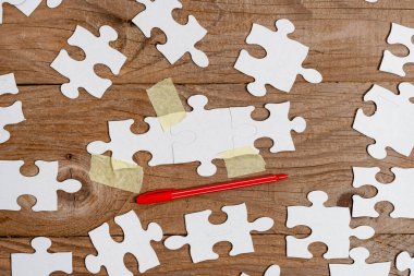 Yakın çekim beyaz testere desenli yapboz parçaları, kayıp parçalarla ilişkilendirilecek. Düz bir zeminde farklı doku ve kağıt aksesuarları ile yerleştirilmiş.