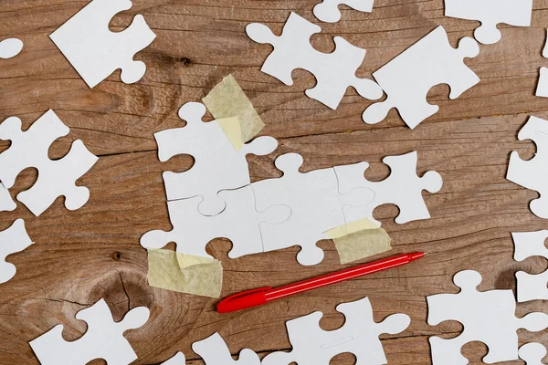 Close-Up White Jigsaw Pattern Puzzle Pieces To Be Connected With Missing Last Piece Positioned On A Flat Lay Background With Different Texture And Paper Supplies Accesories — Stock Photo, Image