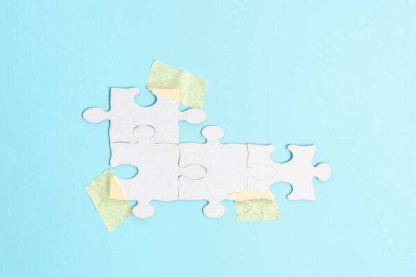 Close-Up White Jigsaw Pattern Puzzle Pieces To Be Connected With Missing Last Piece Positioned On A Flat Lay Background With Different Texture And Paper Supplies Accesories