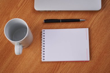 Kalem ve kahve fincanlarıyla dolu boş bir günlüğün yanına kapatılmış bir laptop. Boş Notepad Ballpen ile Not Defteri Bilgisayarı Çalışma masasının üzerine yerleştirilmiş.