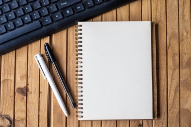 Ahşap masanın üstündeki klavye kalemlerinin yanında boş kırpılmış günlük. Masanın üzerine yerleştirilmiş Klip ve Kalemlerle Boş Notepad Aç.