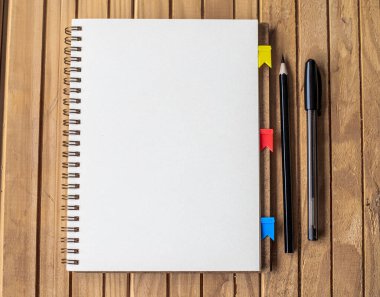 Ahşap masanın üstünde boş kırpılmış kalemlerin olduğu bir günlük. Masaya yerleştirilmiş Klip ve Farklı Kalemlerle Boş Notepad Aç.
