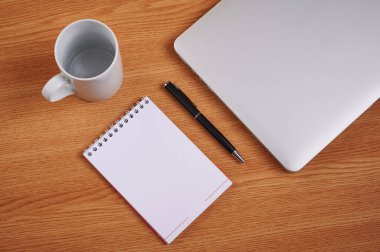 Kalem ve kahve fincanlarıyla dolu boş bir günlüğün yanına kapatılmış bir laptop. Boş Notepad Ballpen ile Not Defteri Bilgisayarı Çalışma masasının üzerine yerleştirilmiş.