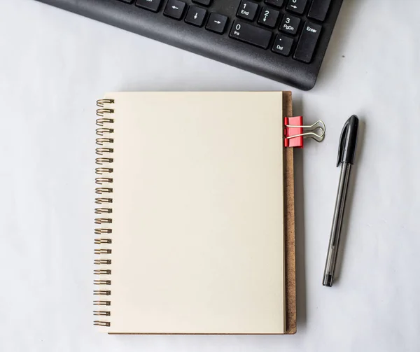 Prázdné otevřené oříznuté deník vedle klávesnice pero na vrcholu dřevěného stolu. Prázdný otevřený poznámkový blok s klipem a tužkou umístěný u klávesnice na stole. — Stock fotografie