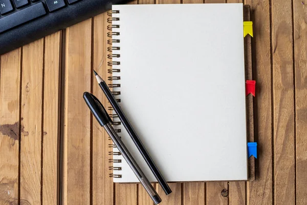 Journal clippé ouvert vide à côté d'un stylos à clavier sur le dessus du bureau en bois. Bloc-notes ouvert vierge avec clip et crayons près du clavier placé sur la table. — Photo