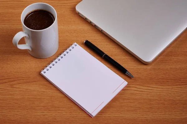 Lezárt Laptop mellett üres Journal tollal és kávésbögrével át asztal. Notebook számítógép üres jegyzettömbbel Ballpen mellett kupa felett elhelyezett munkaasztal. — Stock Fotó