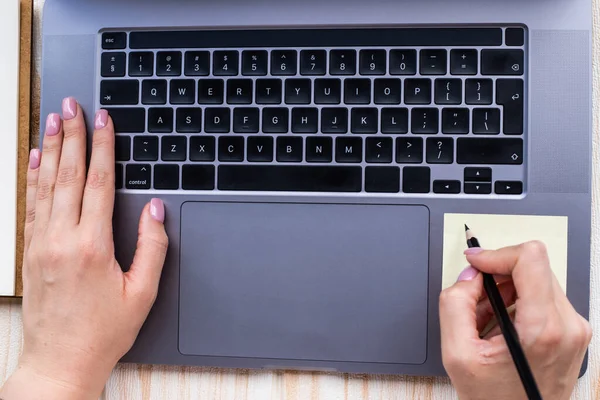 Mains appuyant sur les touches du clavier de l'ordinateur tout en écrivant avec un crayon dans le bloc-notes. Palmiers dactylographiant le clavier de carnet et écrivant le crayon sur le papier. — Photo