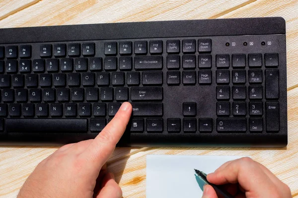 Manos presionando teclas del teclado de la computadora mientras se escribe con lápiz en el bloc de notas. Palmeras tecleando el teclado del cuaderno y escribiendo lápiz sobre papel. —  Fotos de Stock
