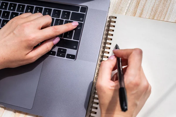 Mains appuyant sur les touches du clavier de l'ordinateur tout en écrivant avec un crayon dans le bloc-notes. Palmiers dactylographiant le clavier de carnet et écrivant le crayon sur le papier. — Photo