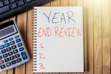 Kavramsal Görünüm Yıl Sonu İncelemesi. Yıllık başarı ve hedef geliştirme değerlendirmesi üzerine yazılan sözcük Hesap Makinesi Klavyesi Tablo Üzerine yerleştirilmiş Boş Spiral Not Defteri.