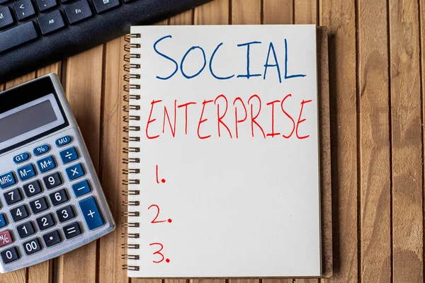 Inspirace ukazuje znamení Sociální Enterprise. Obchodní vitrína Jedná se o podnik, který má specifické civilní cíle Prázdný Otevřít spirálu notebook s kalkulačka klávesnice pero umístěn přes stůl. — Stock fotografie