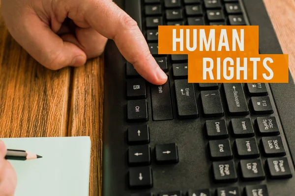 Text sign showing Human Rights. Business showcase the equality of fighting for your rights individuality Hands Pressing Computer Keyboard Keys While Writing With Pencil In Notepad.