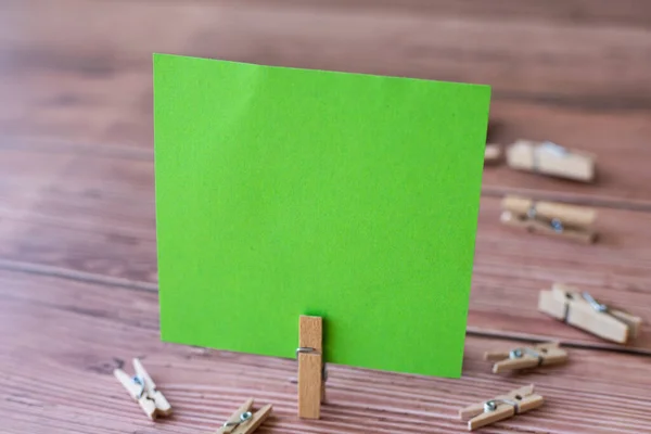 Nota quadrada em branco cercada por clipes de lavanderia mostrando novo significado. Pedaço vazio de papel pegajoso cortado verticalmente colocado em cima da mesa de madeira exibindo ideia fresca. — Fotografia de Stock