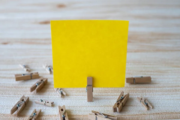 Piece Of Blank Square Note Surrounded By Laundry Clips Showing New Meaning. Empty Sticky Paper Clipped Upright Placed On Top Of Wooden Table Displaying Fresh Idea.