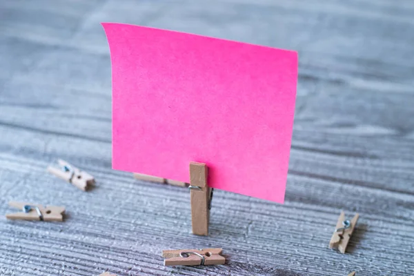 Pedaço de nota quadrada em branco cercado por clipes de lavanderia mostrando novo significado. Papel pegajoso vazio cortado verticalmente colocado no topo da mesa de madeira exibindo ideia fresca. — Fotografia de Stock